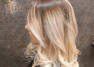 Femme avec cheveux blonds ondulés en salon de coiffure.